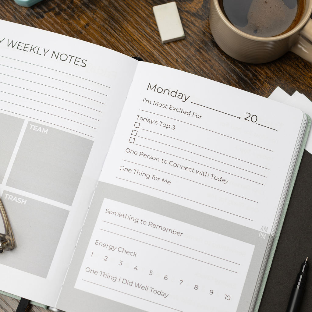 An open weekly TEACHERTIME teacher wellness journal planner page on a dark wooden desk, surrounded by a coffee cup, a small notepad, and pen.